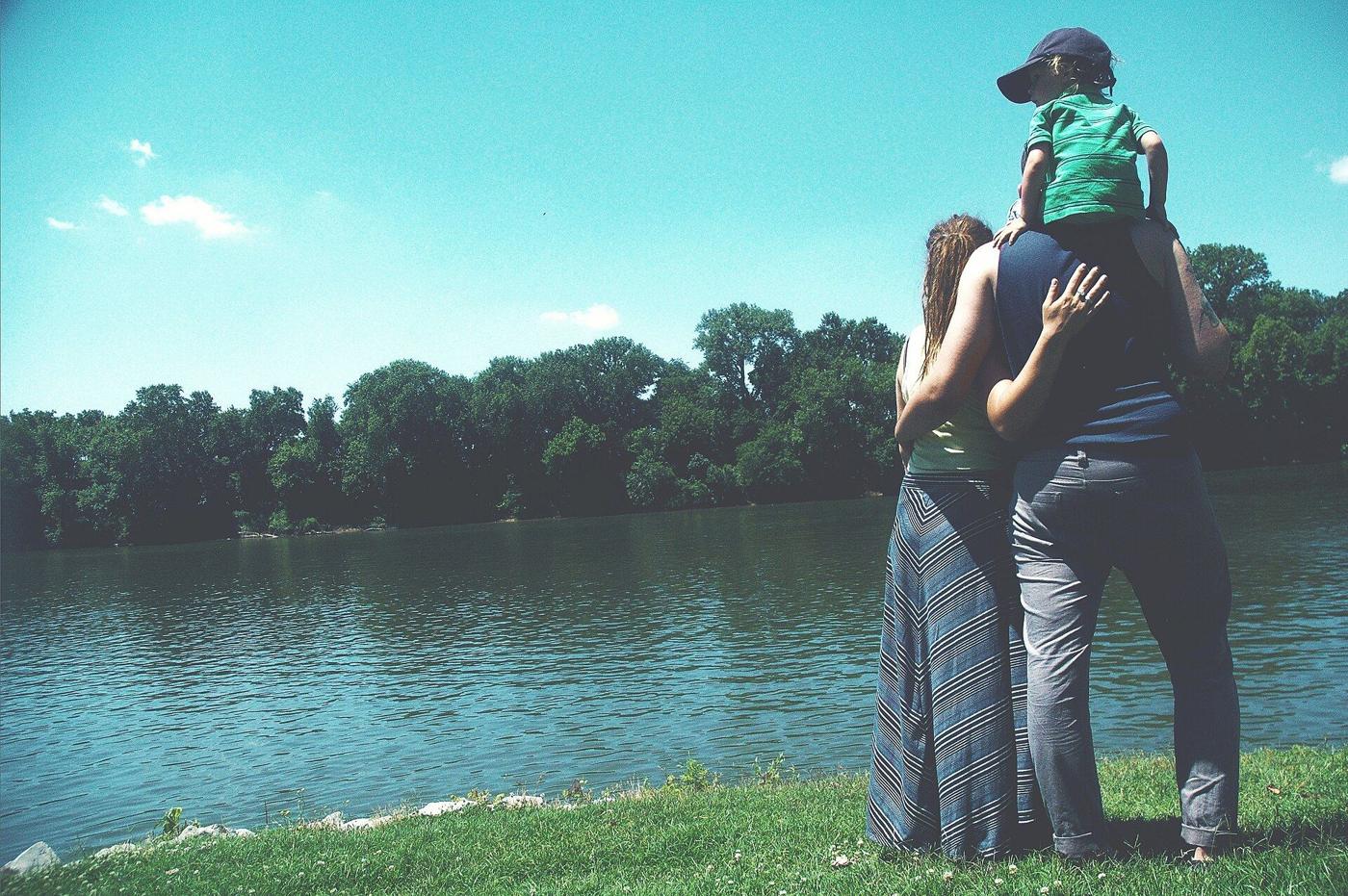 A parent holding a child on their shoulders, looking out over a lake