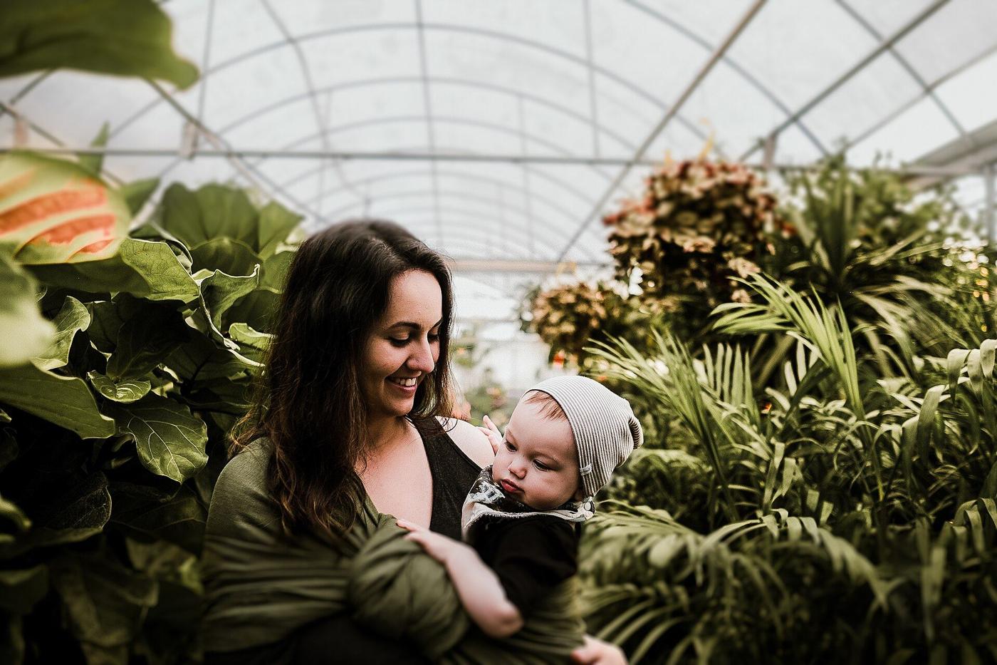 A mother smiling at her baby in a bright greenhouse